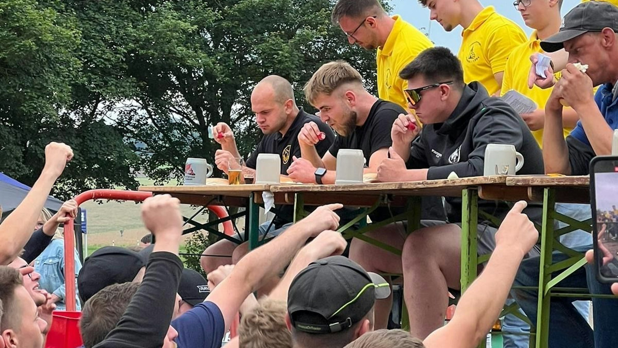 Vier Männer sitzen an einem Tisch und essen, das Publikum feuert sie an.