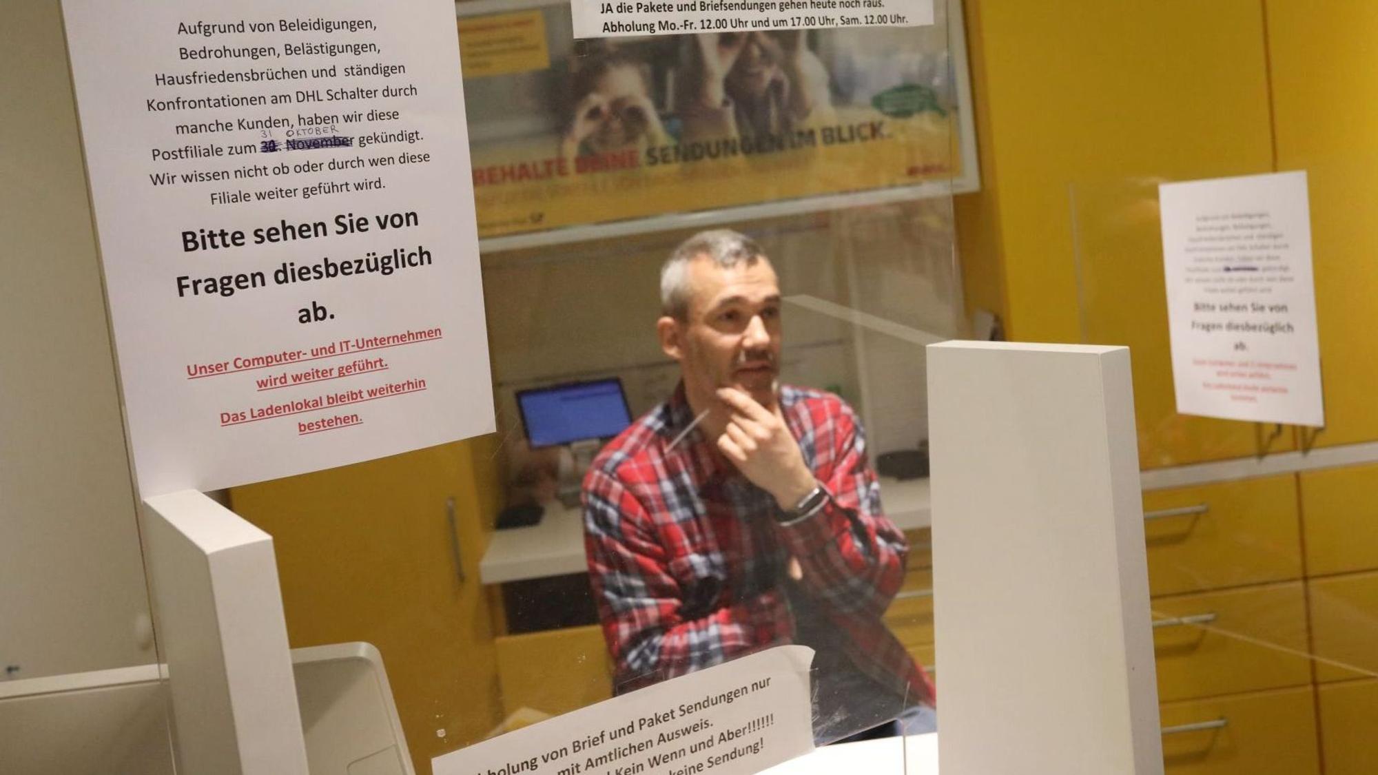 Ein Mann in kariertem Hemd sitzt hinter einem Schalter der Postfiliale in Königswinter.