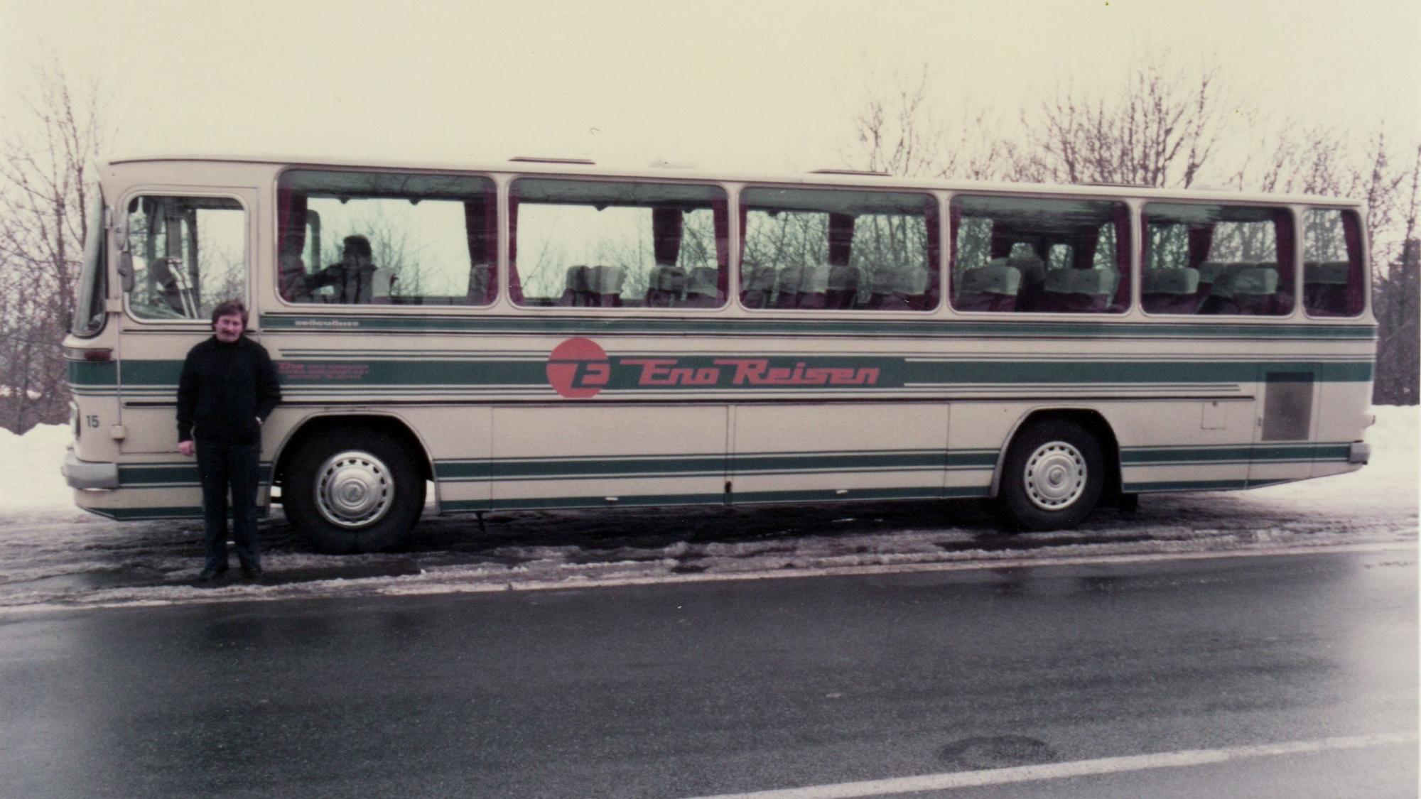 Ein alter Reisebus auf winterlicher Straße, davor steht der Fahrer.