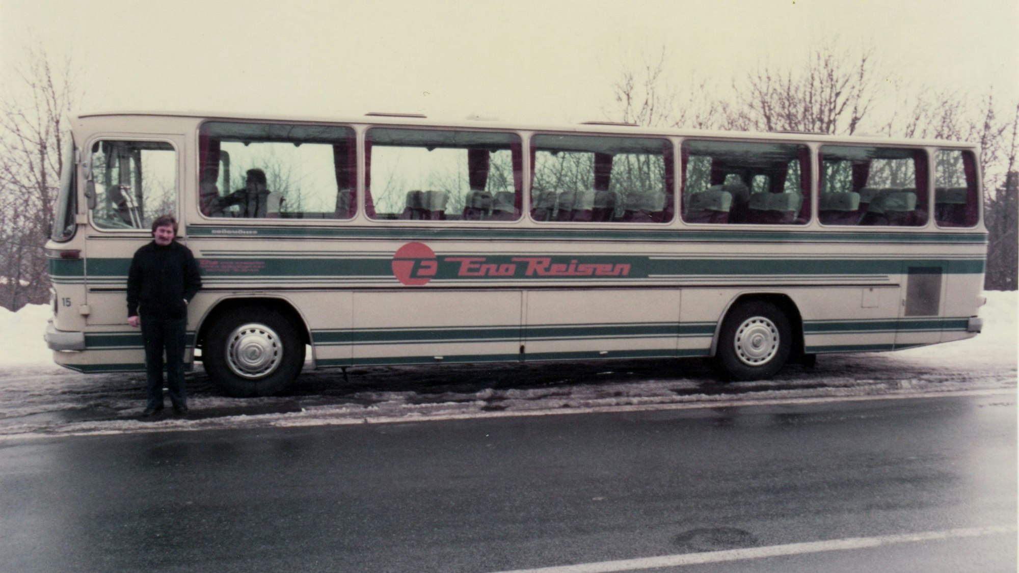 Ein alter Reisebus auf winterlicher Straße, davor steht der Fahrer.