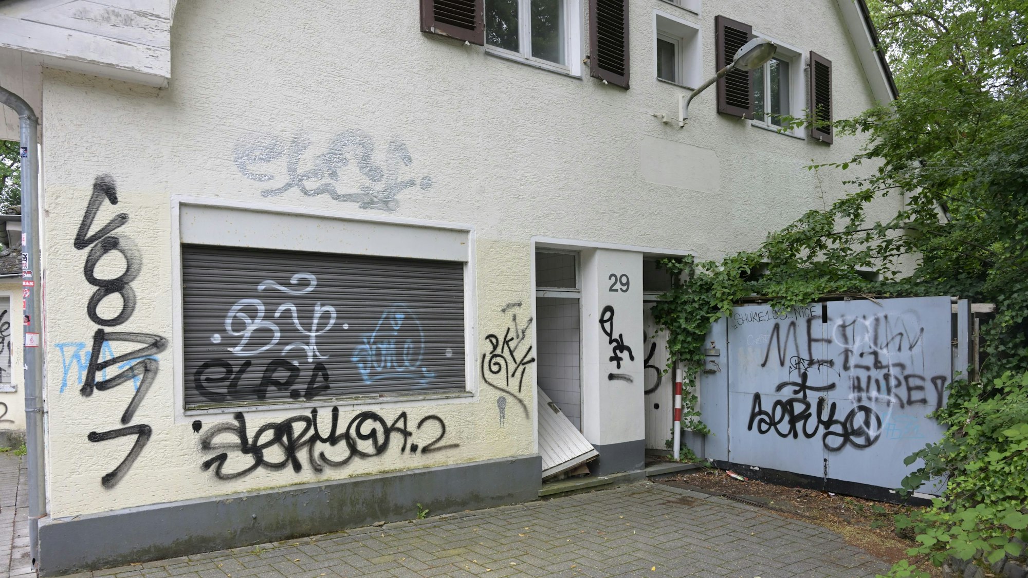 Zu sehen ist die beschmierte Fassade des Gebäudes und die eingetretene Tür.
