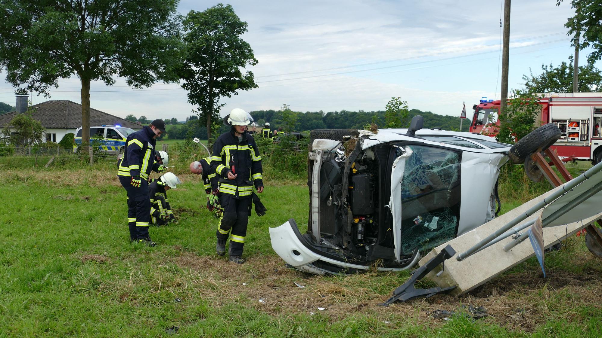 Feuerwehrleute stehen auf einer Wiese neben einem zerstörten Auto.