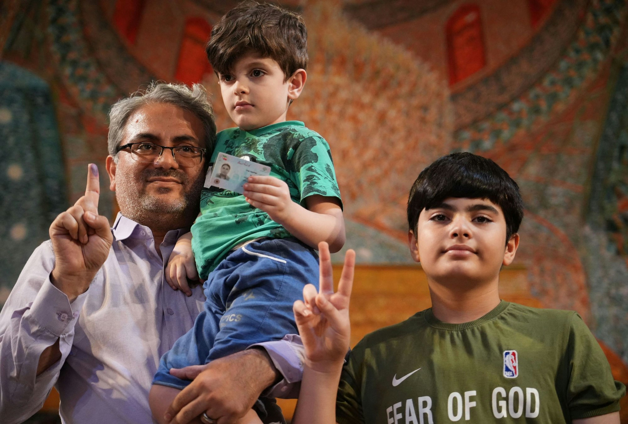 An Iranian man shows off his ink-stained finger as he poses with his sons at a polling station, in Tehran on July 5, 2024. Polls opened on July 5 for Iran's runoff presidential election, the interior ministry said, pitting reformist candidate Masoud Pezeshkian against ultraconservative Saeed Jalili in the race to succeed Ebrahim Raisi, who died in a May helicopter crash. (Photo by RAHEB HOMAVANDI / AFP)