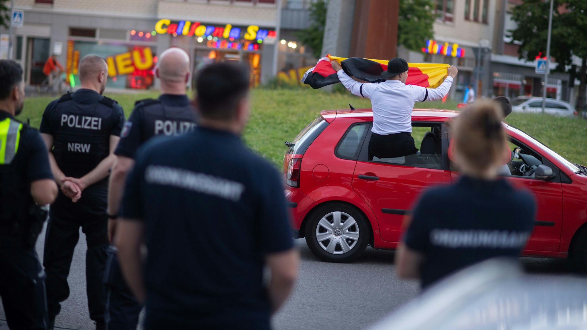Das Bild zeigt einige Polizeibeamte und Mitarbeiter des Ordnungsamts am Europa-Kreisel. Im Hintergrund dreht ein Auto eine Ehrenrunde.