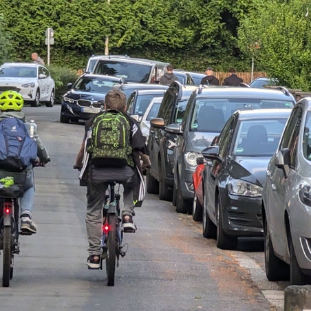 Zwei Kinder mit Rucksäcken auf dem Rücken fahren nebeneinander mit Fahrrädern über die Bonnstraße.