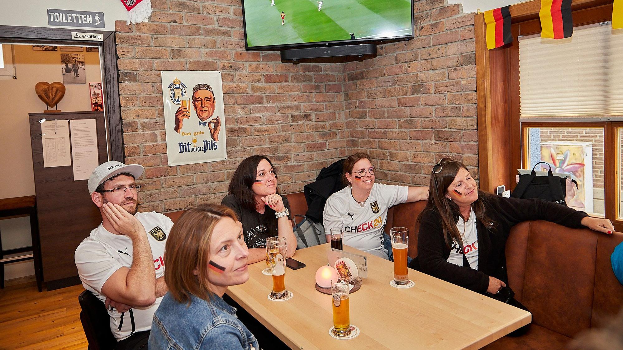 Das Bild fünf Deutschlandfans im Saal Gier, wie sie das Spiel auf einem Fernseher verfolgen.