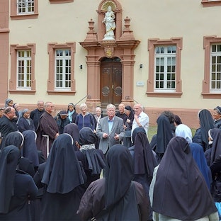 Viele weibliche Ordensgeistliche stehen im Innenhof des Klosters Steinfeld und lauschen einem Vortrag.