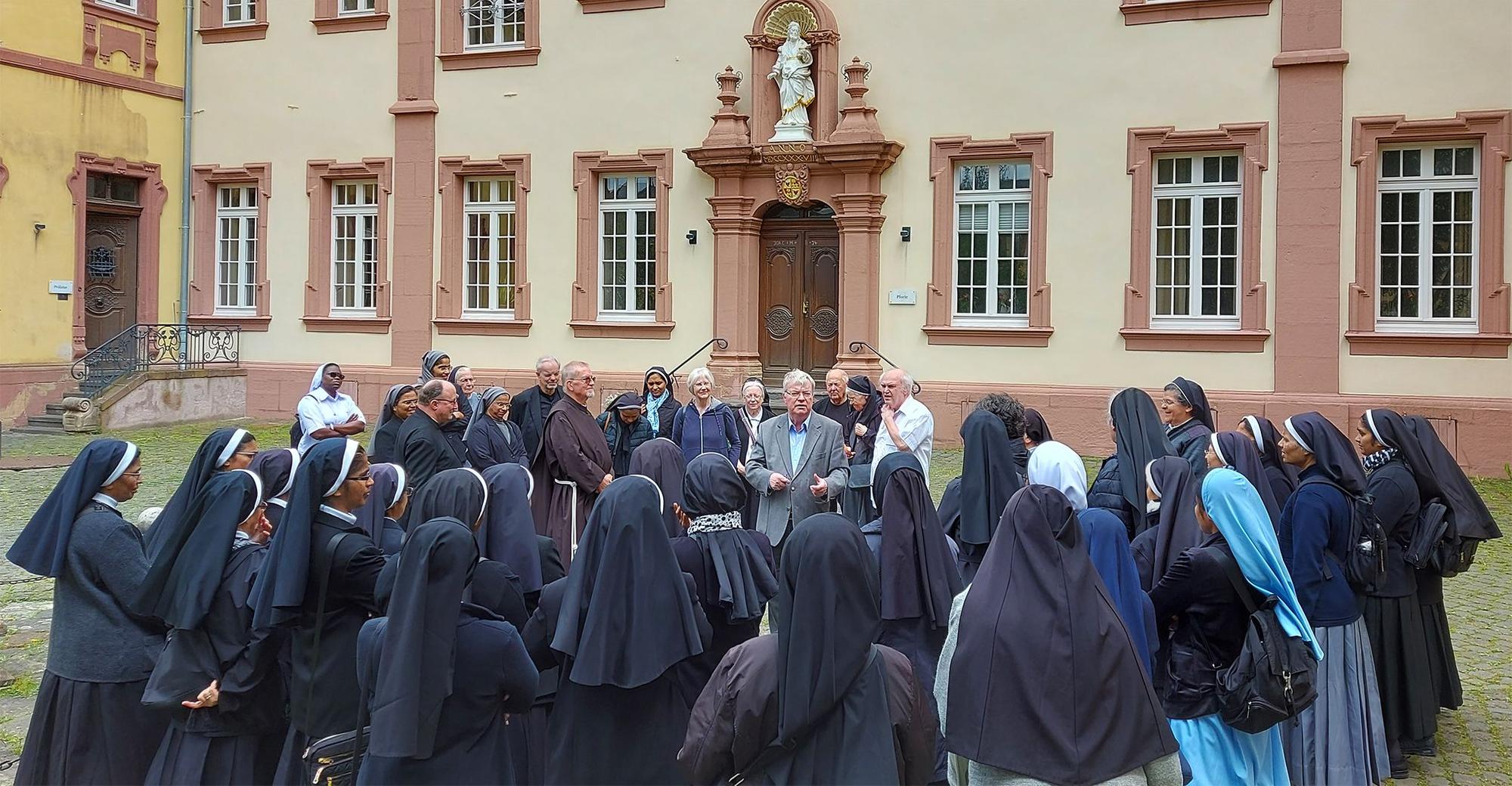 Viele weibliche Ordensgeistliche stehen im Innenhof des Klosters Steinfeld und lauschen einem Vortrag.