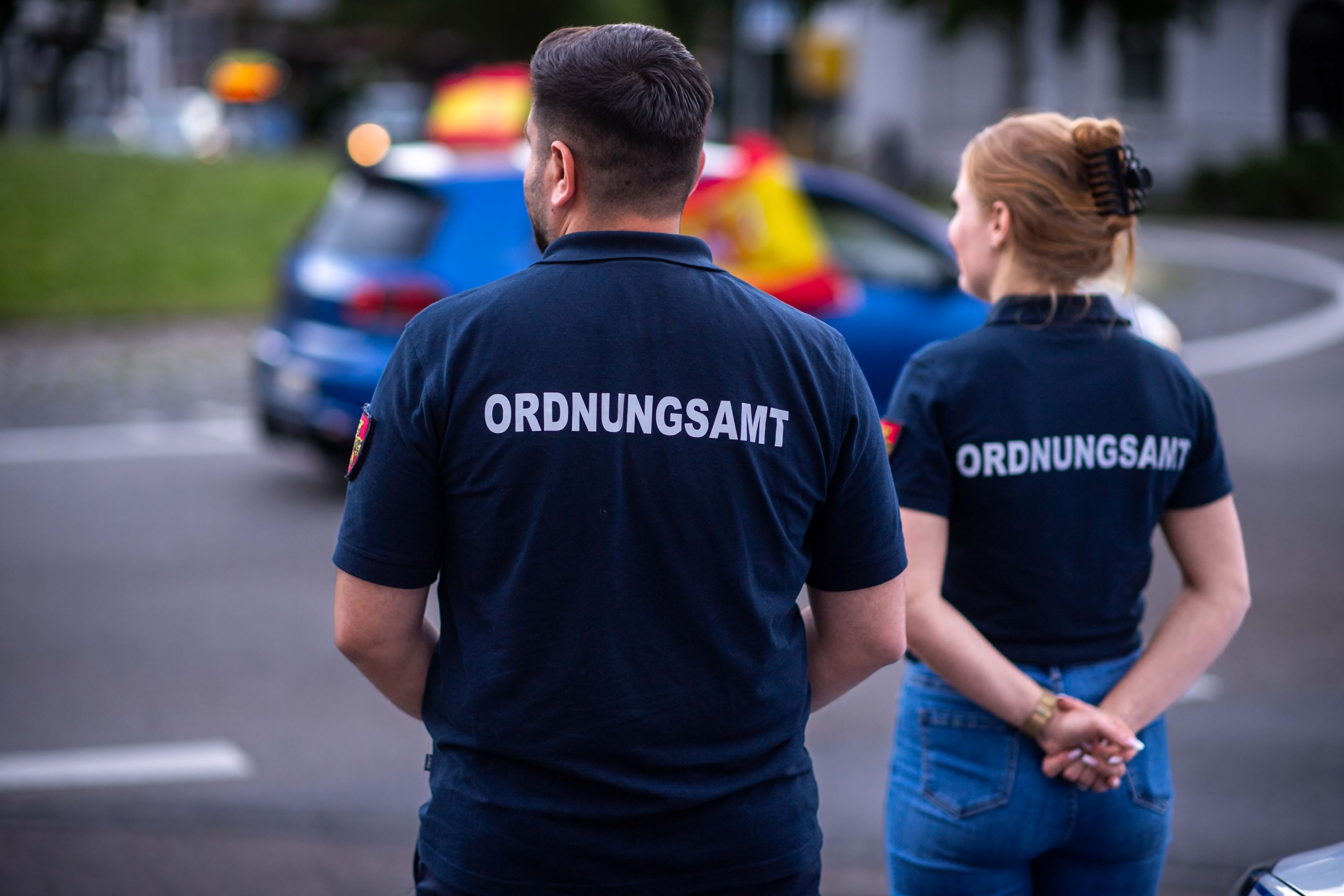 Das Archivbild zeigt zwei Ordnungsamt-Mitarbeiter, die sich in Euskirchen den Autokorso der Spanier nach dem Sieg gegen Deutschland bei der EM 2024 anschauten.