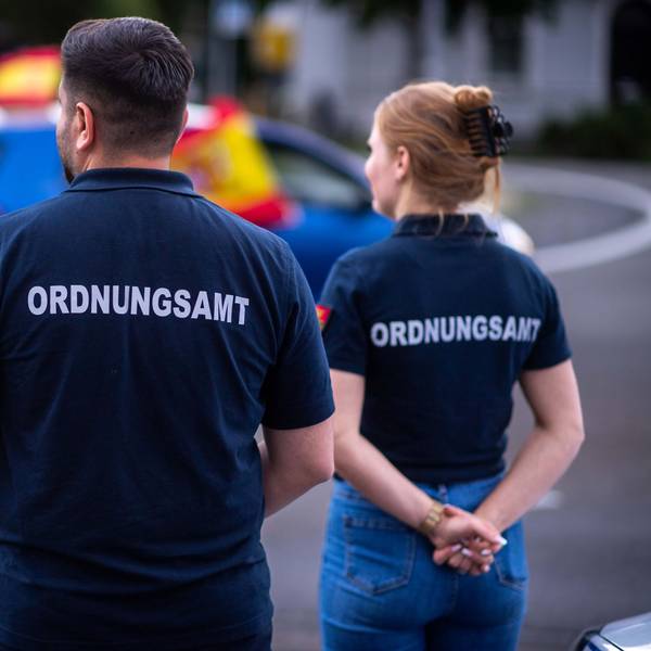 Das Archivbild zeigt zwei Ordnungsamt-Mitarbeiter, die sich in Euskirchen den Autokorso der Spanier nach dem Sieg gegen Deutschland bei der EM 2024 anschauten.