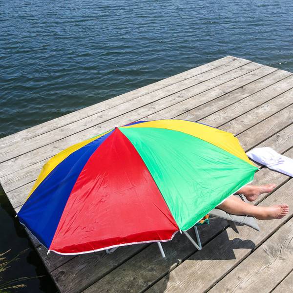 Das Bild zeigt eine Person, die fast komplett unter einem Sonnenschirm liegt, um sich vor den Sonnenstrahlen zu schützen.