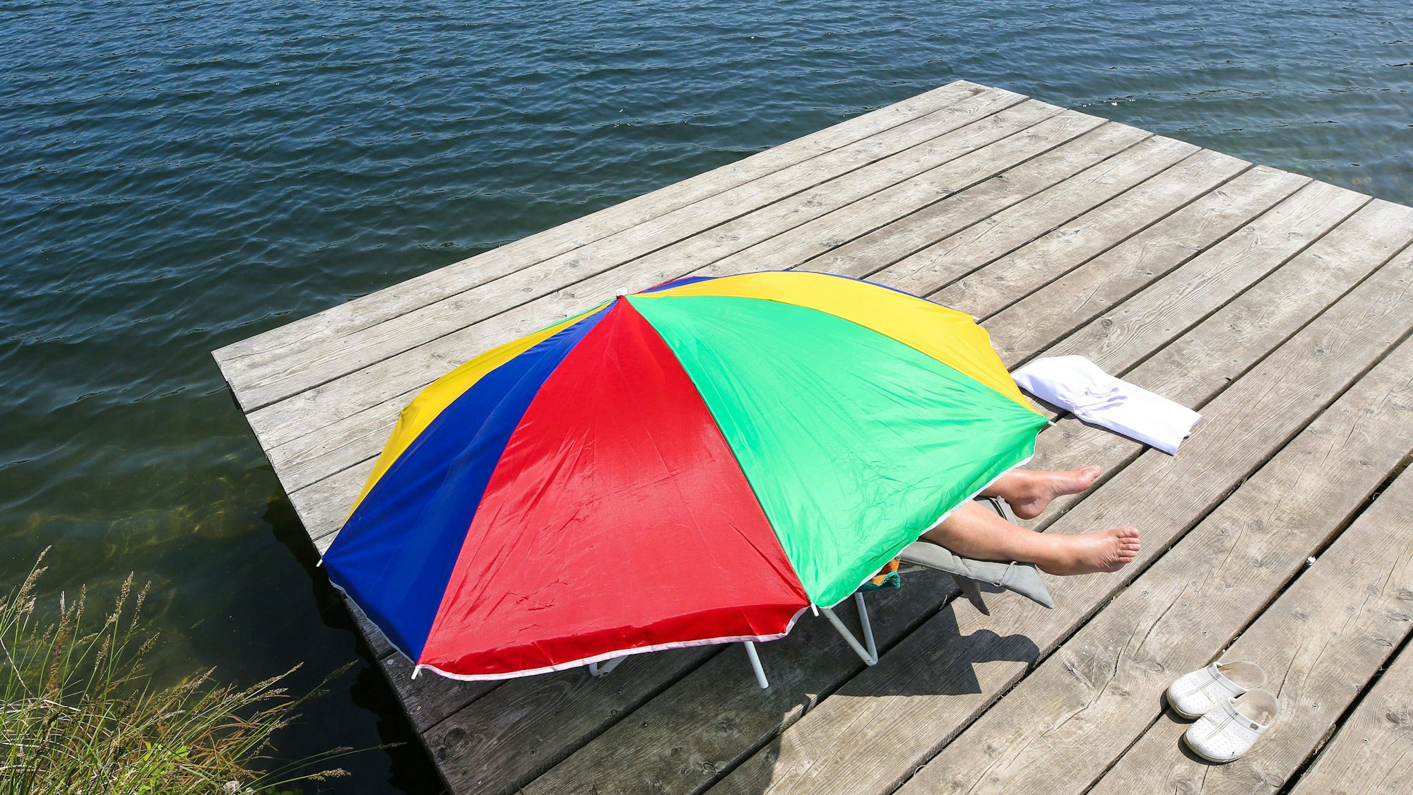 Das Bild zeigt eine Person, die fast komplett unter einem Sonnenschirm liegt, um sich vor den Sonnenstrahlen zu schützen.