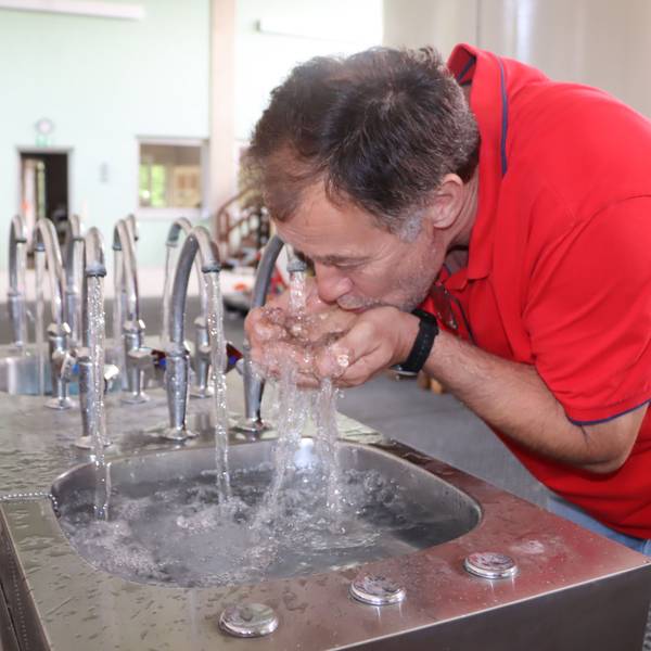 Auf dem Bild ist zu sehen, wie Klaus Evers das Wasser direkt aus den sprudelnden Wasserhähnen im Wasserwerk Wesseling trinkt.