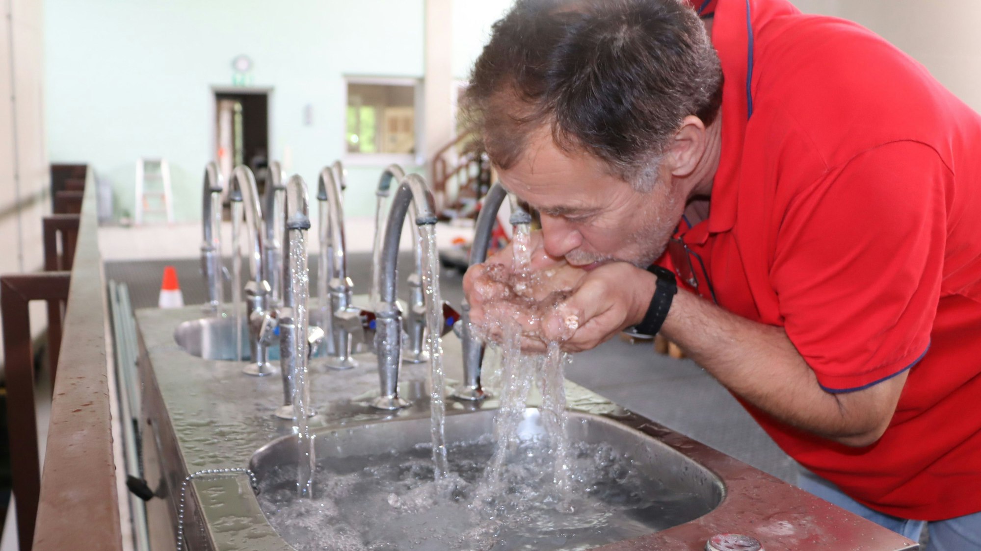 Auf dem Bild ist zu sehen, wie Klaus Evers das Wasser direkt aus den sprudelnden Wasserhähnen im Wasserwerk Wesseling trinkt.