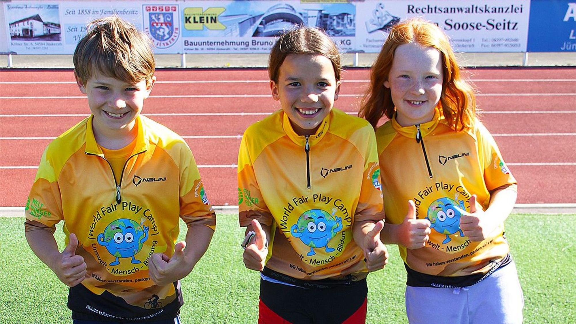 Die Kinder Karl, Frieda und Marie tragen T-Shirt mit dem Logo des „Fair-Play-Camps“.