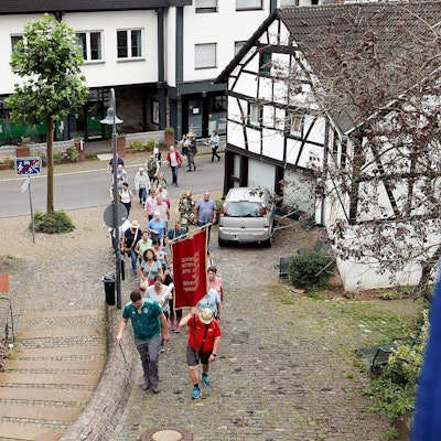 Eine Pilgergruppe geht einen gepflasterten Weg zur Kirche in Heimbach hinauf.