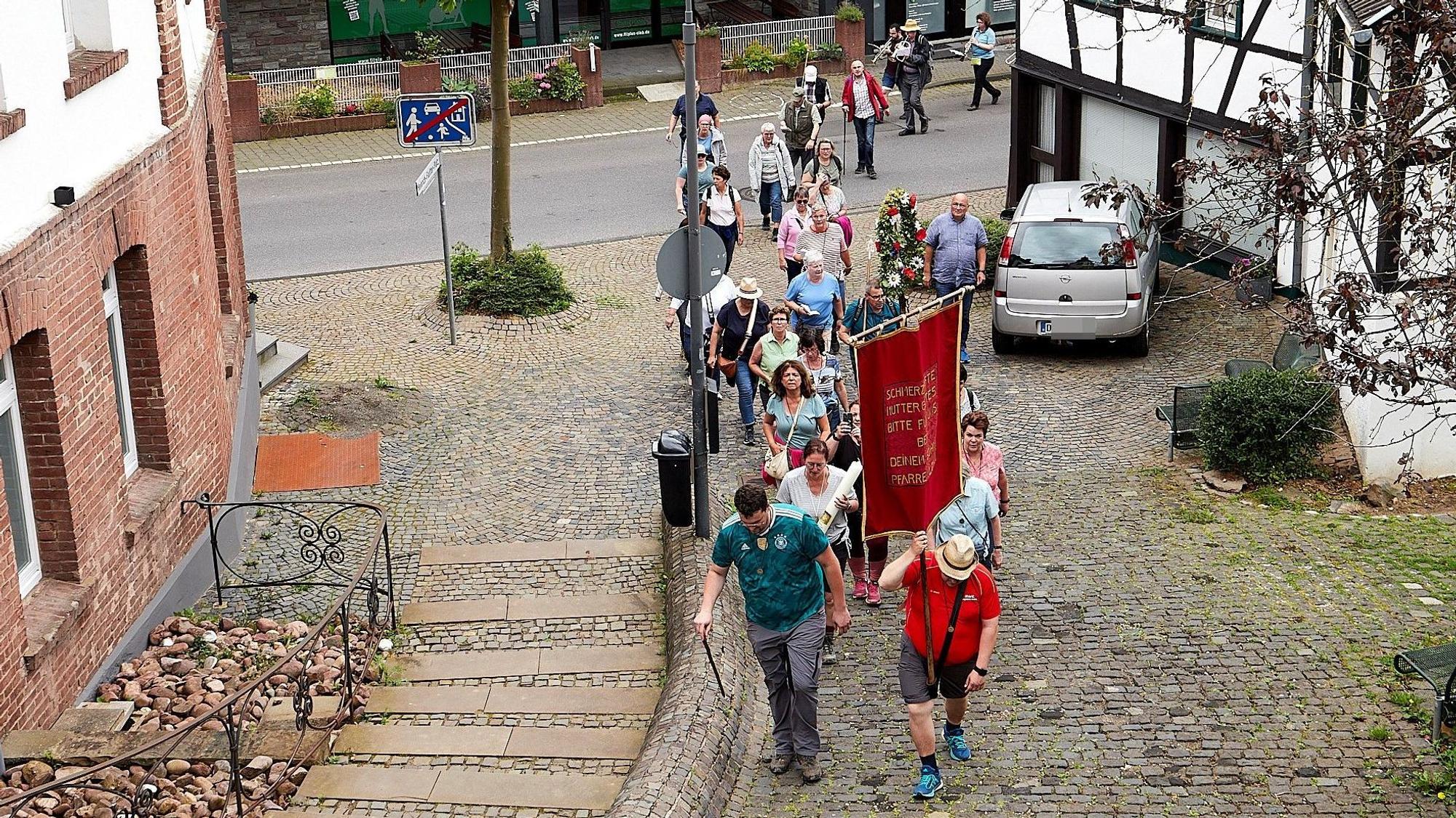 Eine Pilgergruppe geht einen gepflasterten Weg zur Kirche in Heimbach hinauf.