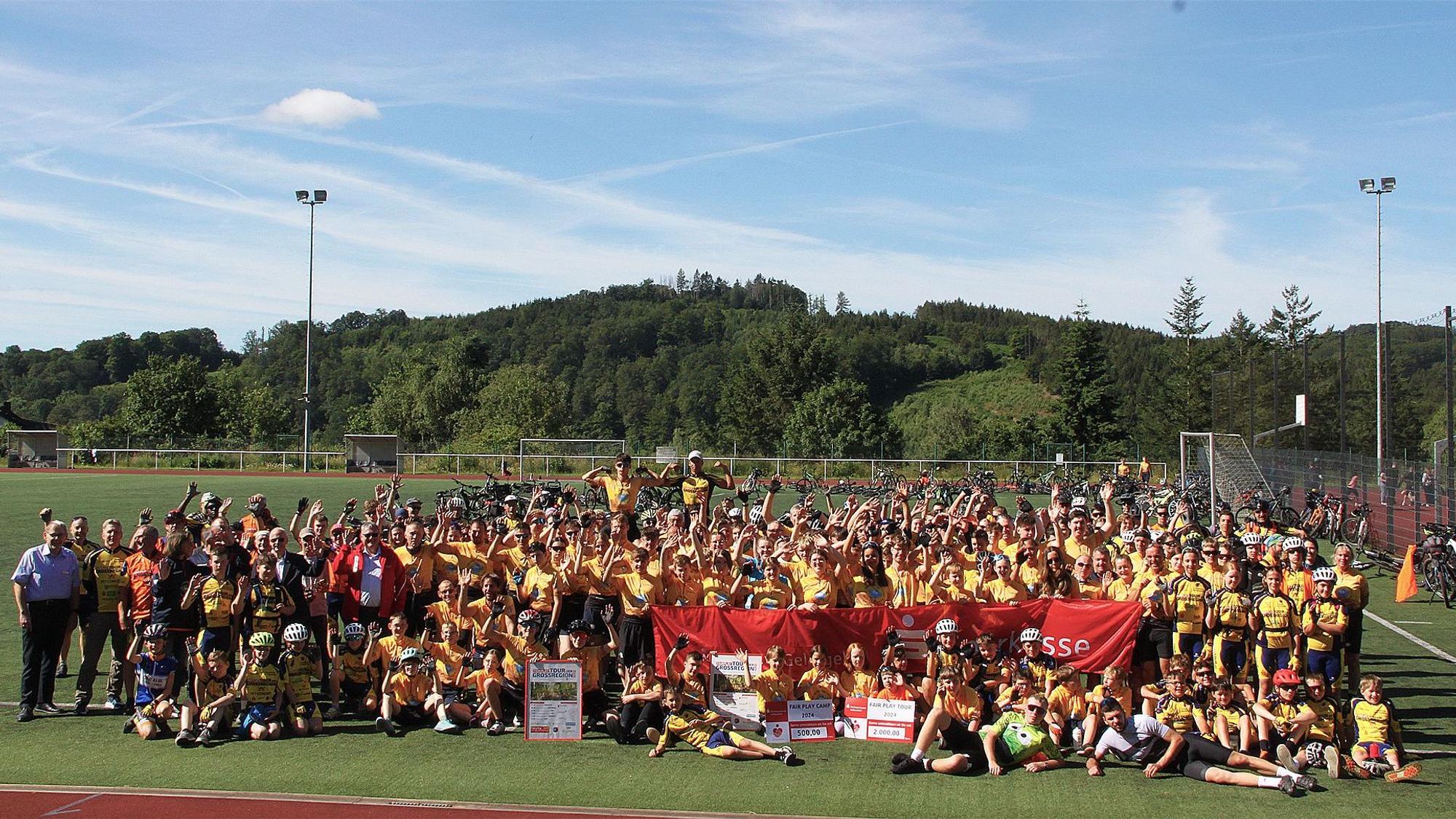 Viele Kinder, Jugendliche und Erwachsene haben sich zum Gruppenbild auf dem Sportplatz versammelt.