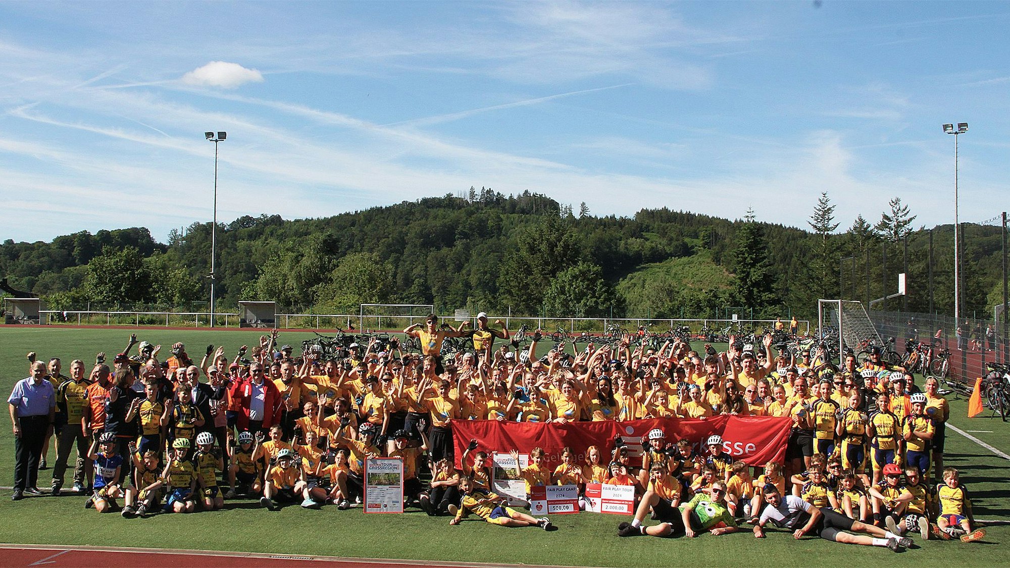 Viele Kinder, Jugendliche und Erwachsene haben sich zum Gruppenbild auf dem Sportplatz versammelt.