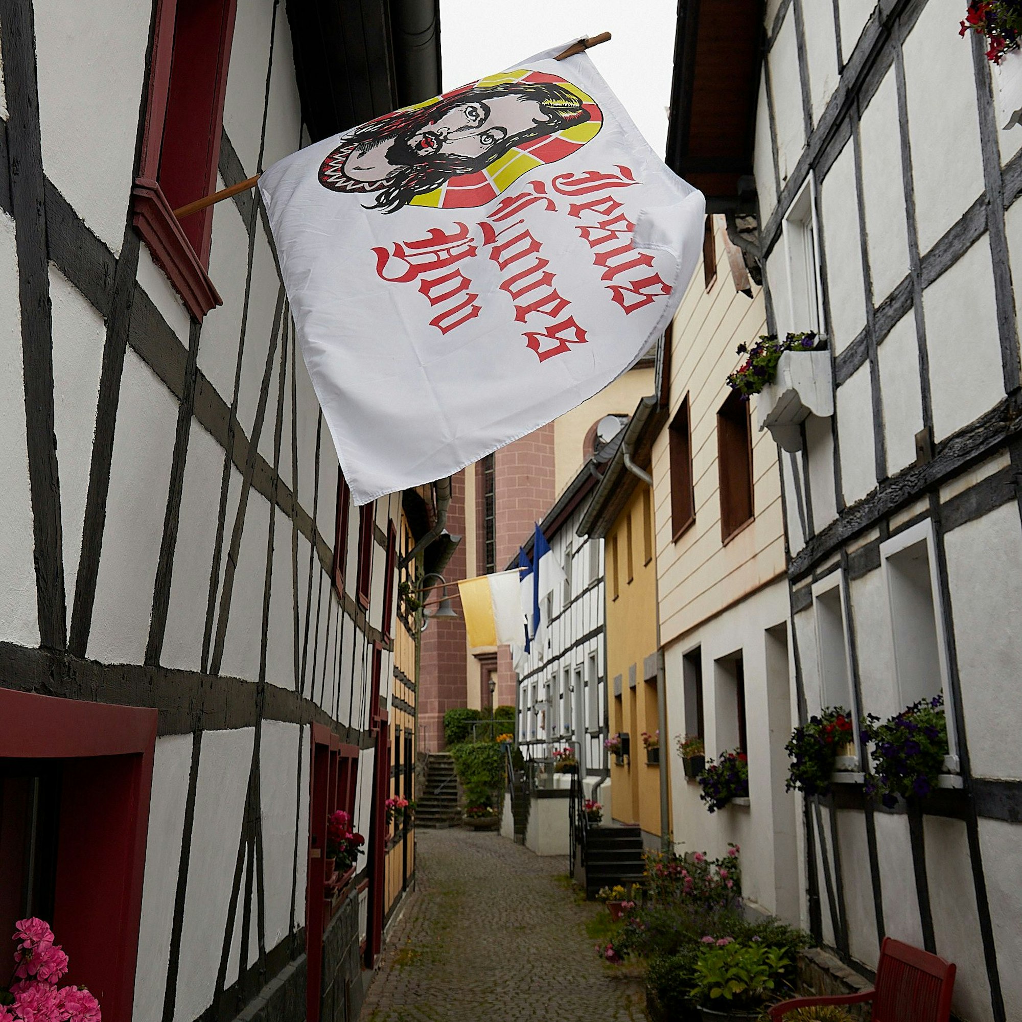 Das Bild zeigt eine Gasse nahe der Kirche in Heimbach. Viele Häuser sind mit Fahnen geschmückt.