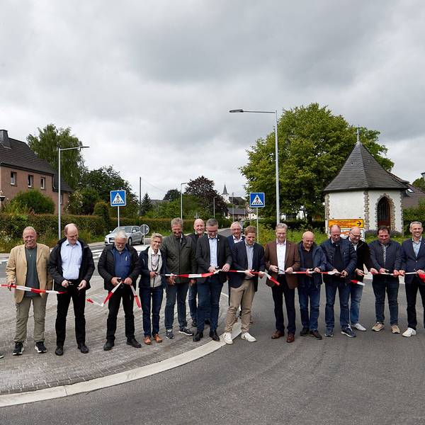 Mehrere Menschen stehen auf der neu hergerichteten Straße und zerschneiden ein rot-weißes Band.