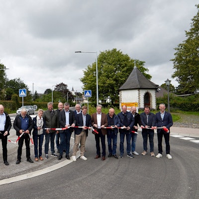 Mehrere Menschen stehen auf der neu hergerichteten Straße und zerschneiden ein rot-weißes Band.