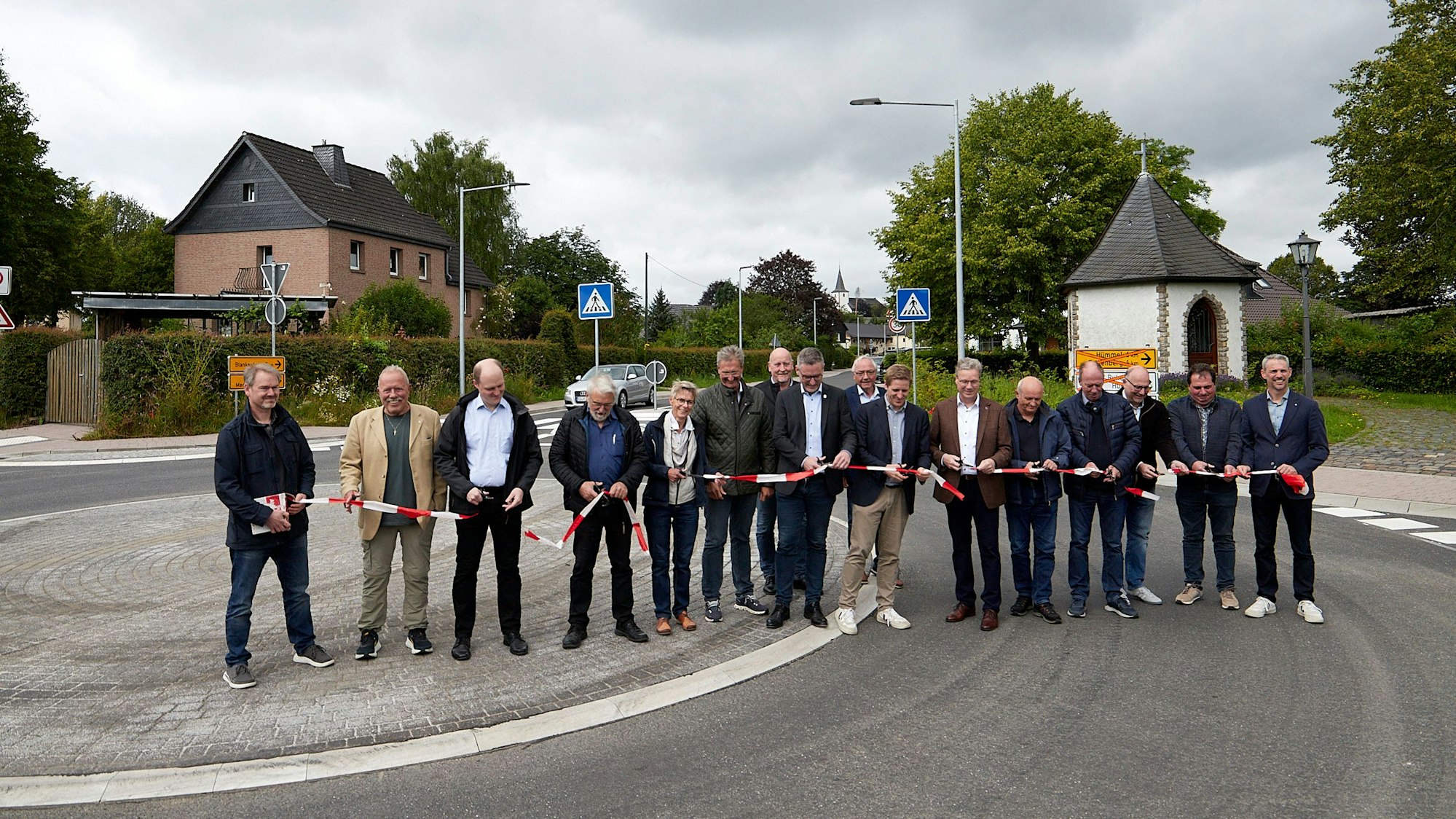 Mehrere Menschen stehen auf der neu hergerichteten Straße und zerschneiden ein rot-weißes Band.