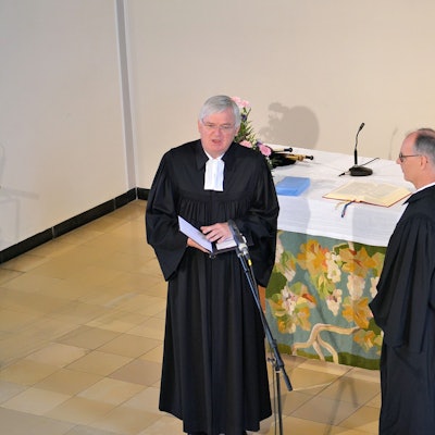 Arnd Prüßmann und Norbert Waschk stehen vor dem Altar der evangelischen Kirche Euskirchen. Waschk spricht in ein Mikrofon.