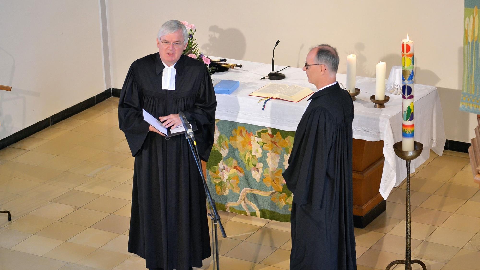 Arnd Prüßmann und Norbert Waschk stehen vor dem Altar der evangelischen Kirche Euskirchen. Waschk spricht in ein Mikrofon.