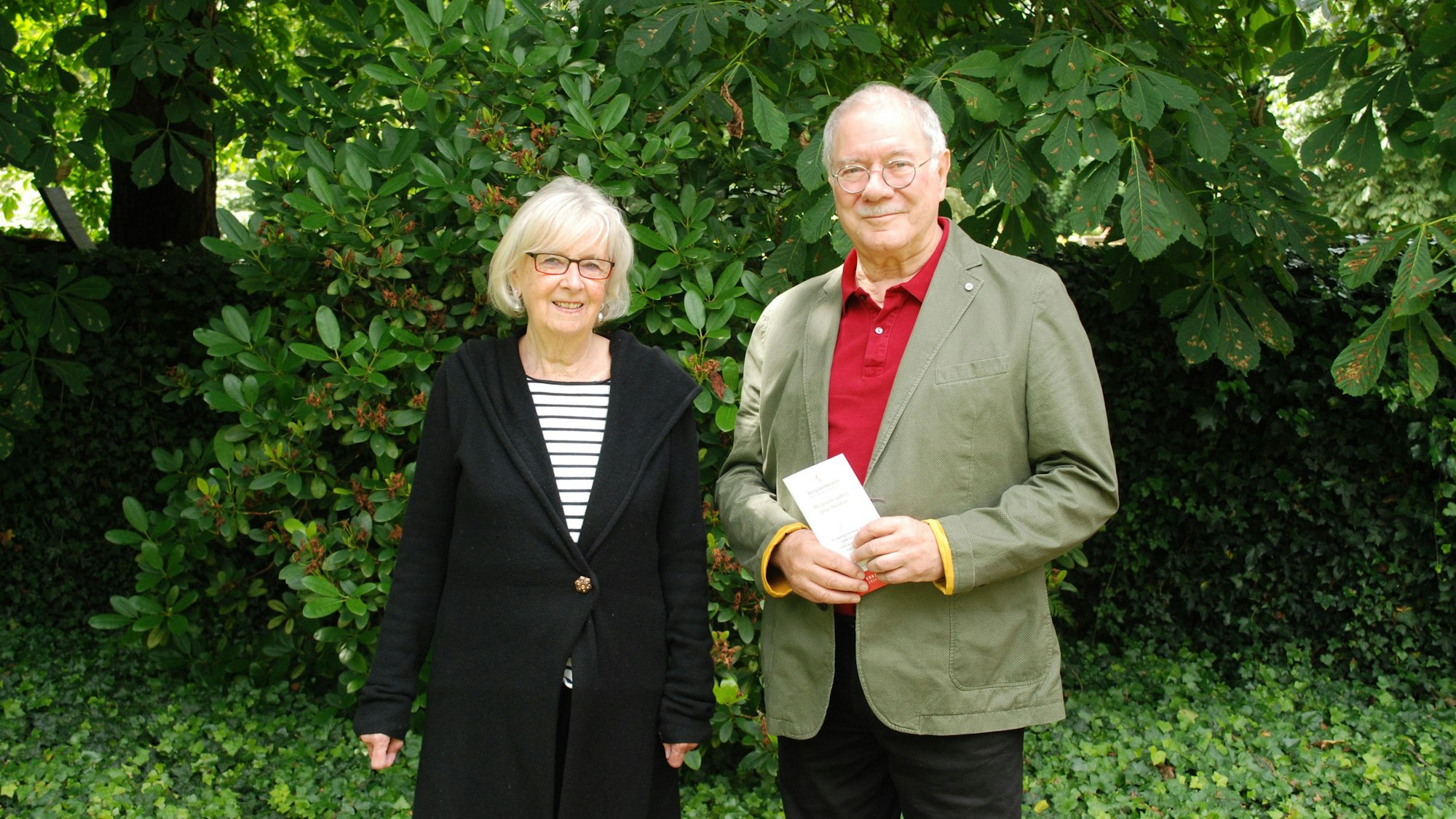 Vera von Schnitzler und Paul Georg Neft stehen nebeneinander vor einer Hecke.