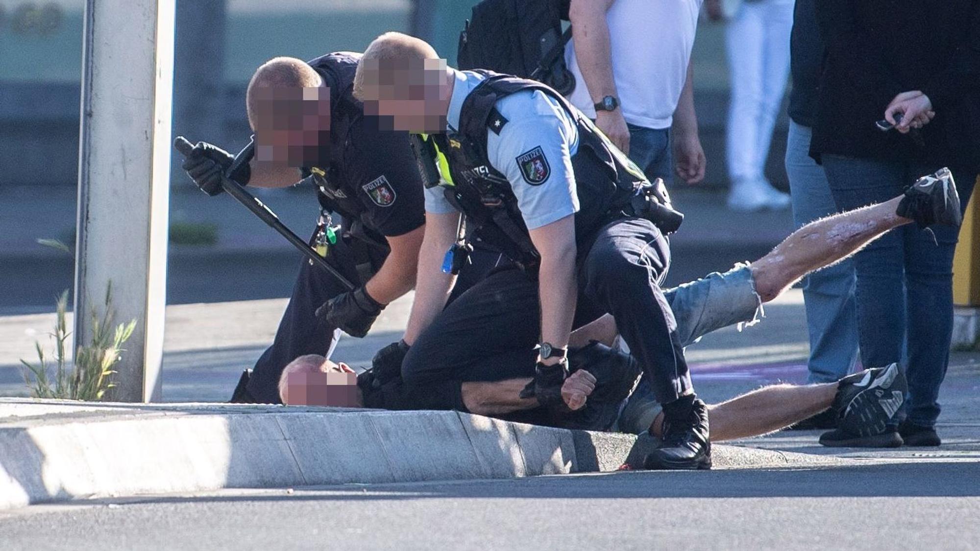 Das Bild zeigt zwei Polizisten, die einen Mann auf den Boden drücken. Der Mann liegt auf dem Bauch.