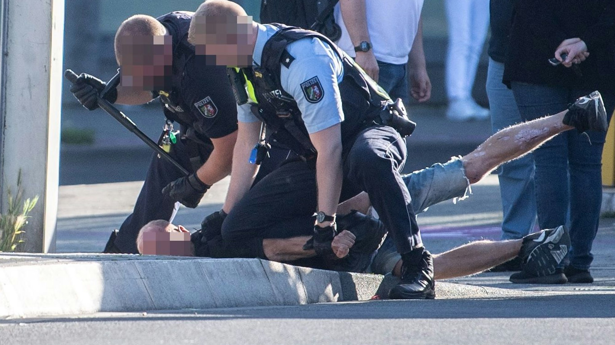 Das Bild zeigt zwei Polizeibeamte, die einen Mann fixieren.