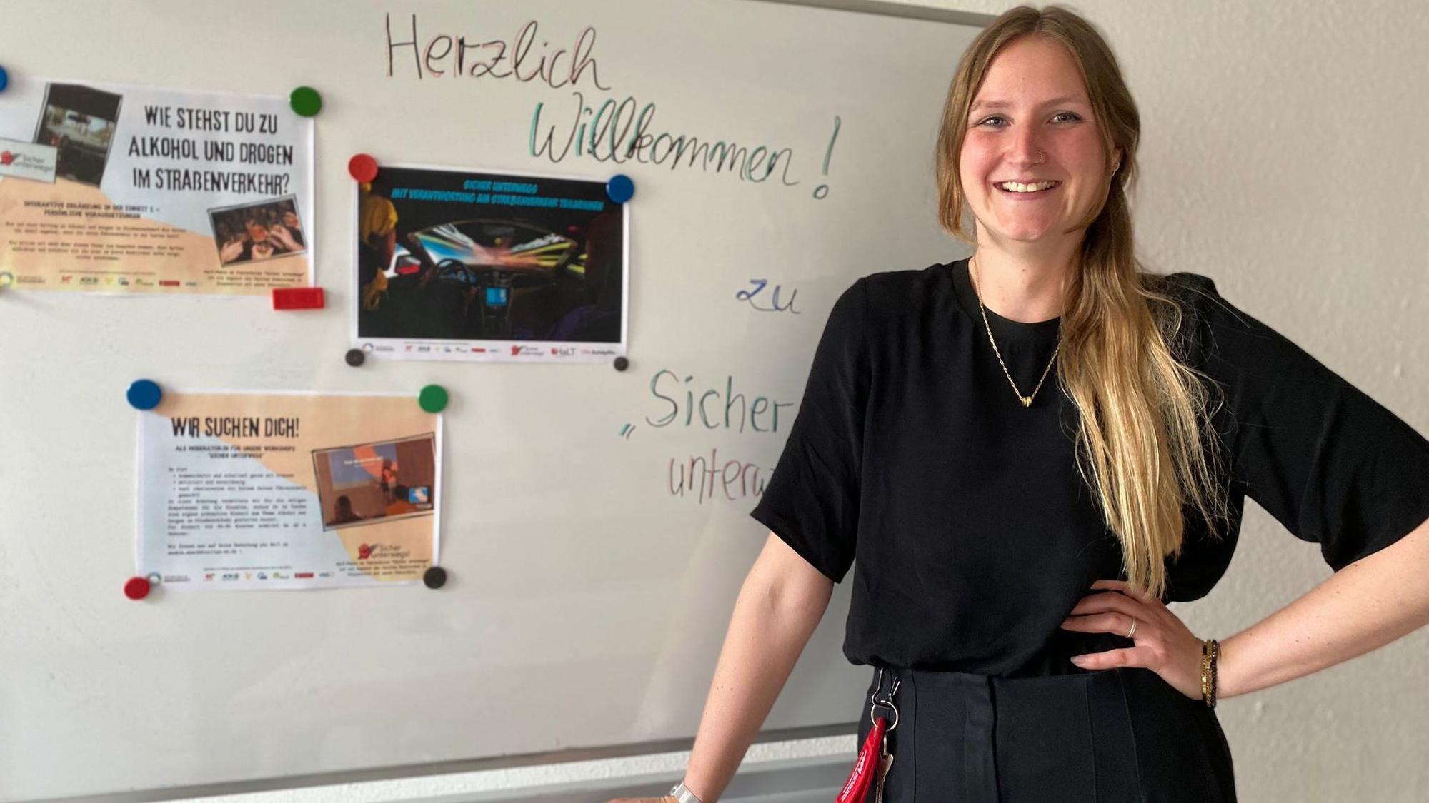 Projektkoordinatorin Saskia Mück posiert vor einem Whiteboard an das Informationsmaterialien für Verkehrssicherheit geheftet sind.