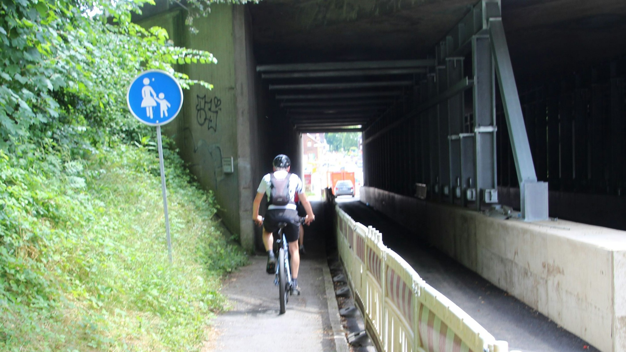 Ein behelmter Radfahrer fährt über einen Fußgängerweg.