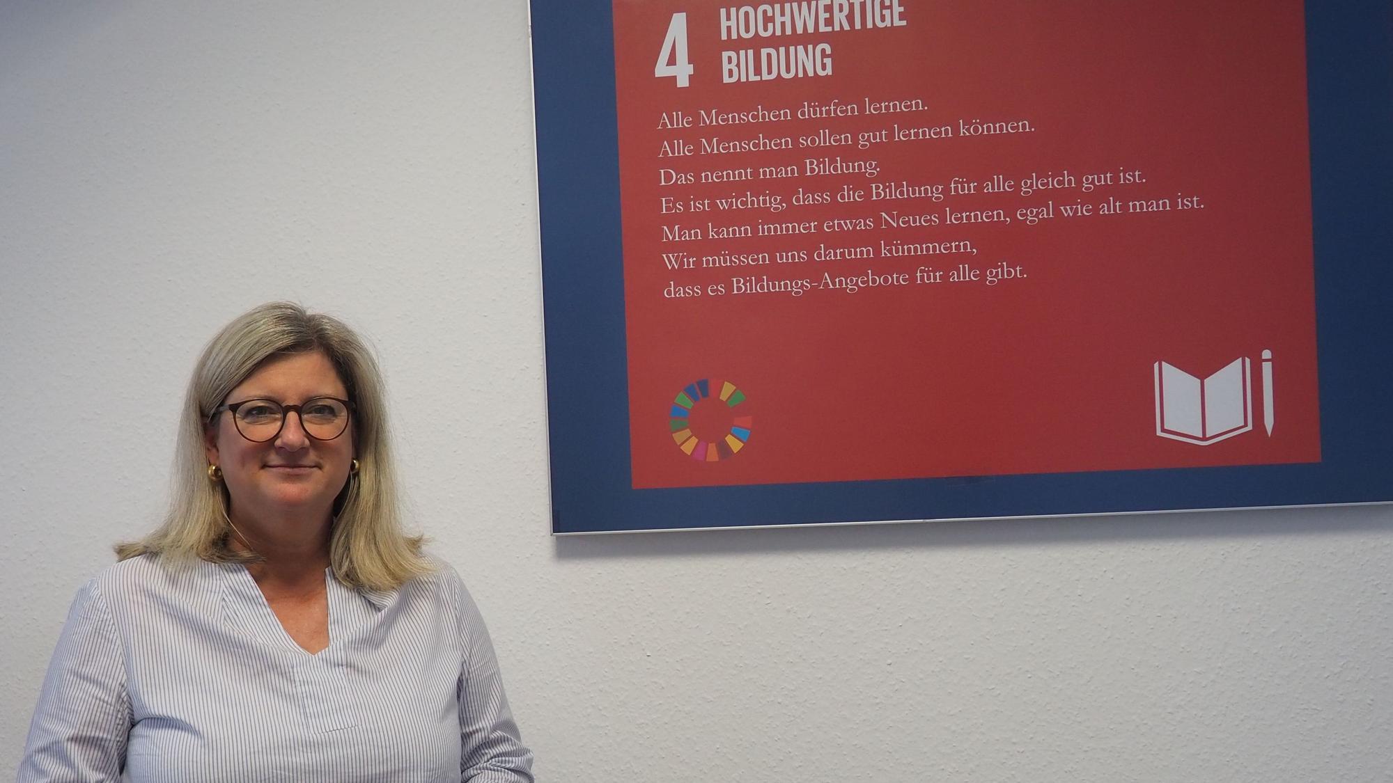 Vanessa Becker steht vor einem Plakat, auf dem der Begriff Bildung erklärt wird..