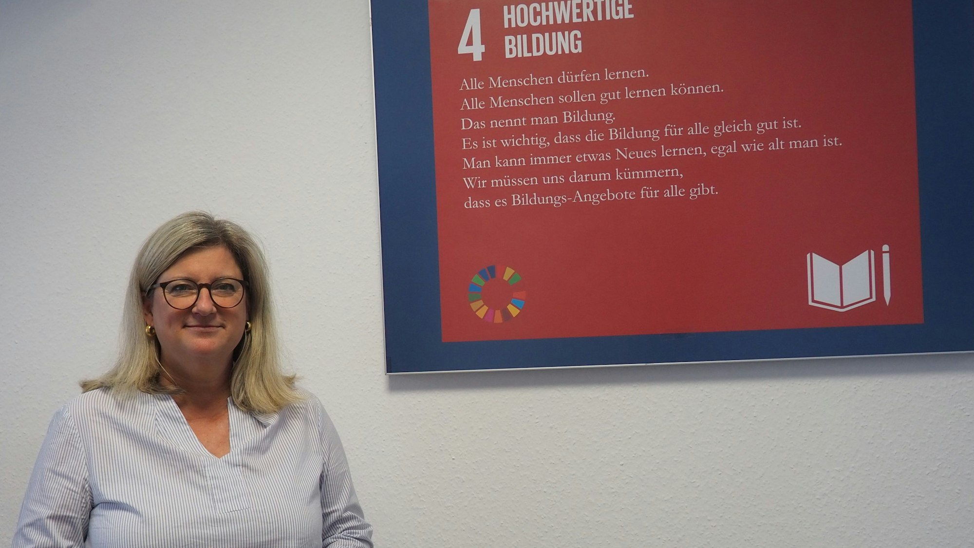 Vanessa Becker steht vor einem Plakat, auf dem der Begriff Bildung erklärt wird..
