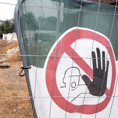 Hinter einem Bauzaun steht eine Planierraupe, um die Abrisskante zu sichern.