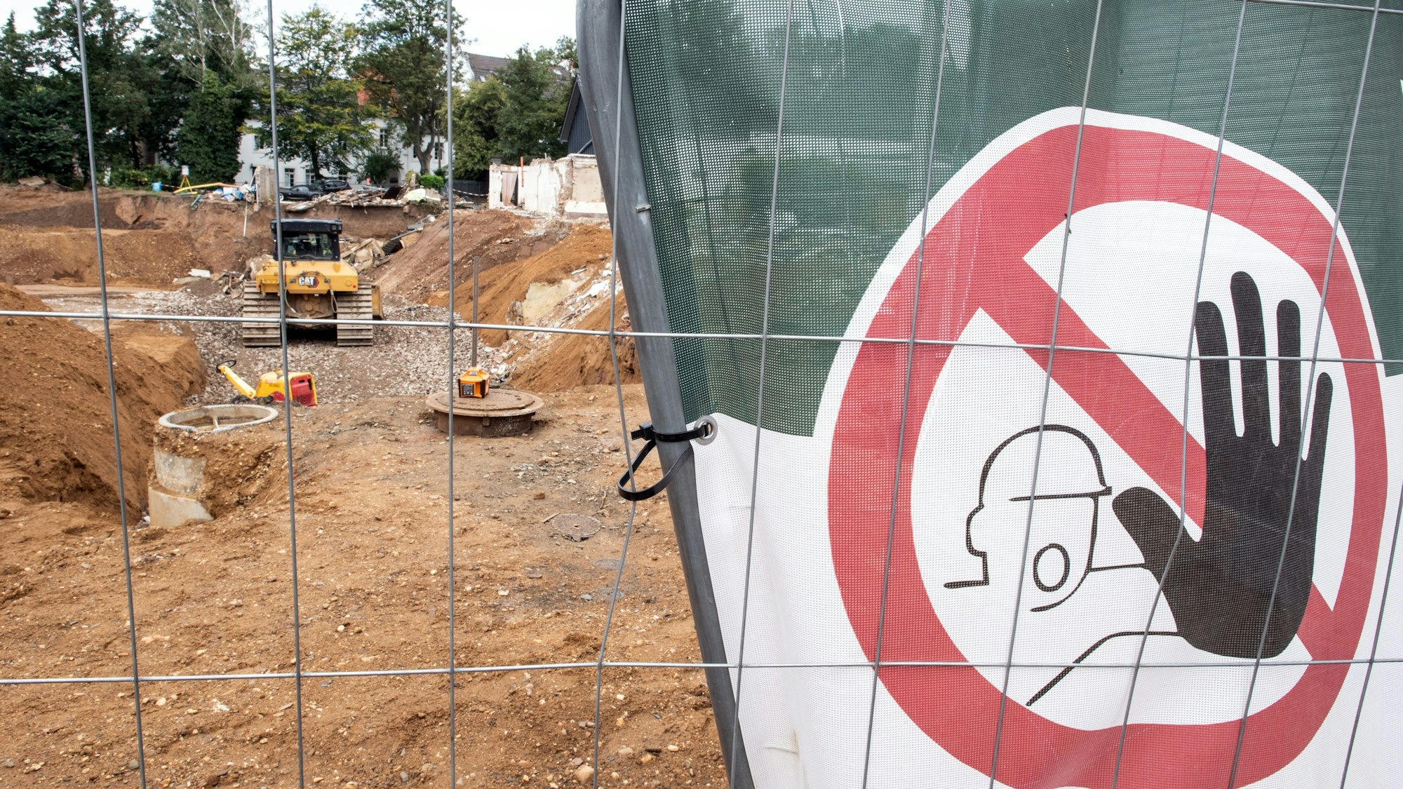Hinter einem Bauzaun steht eine Planierraupe, um die Abrisskante zu sichern.