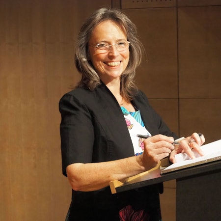 Eine Frau steht an einem Rednerpult und unterschreibt auf einem Papier.