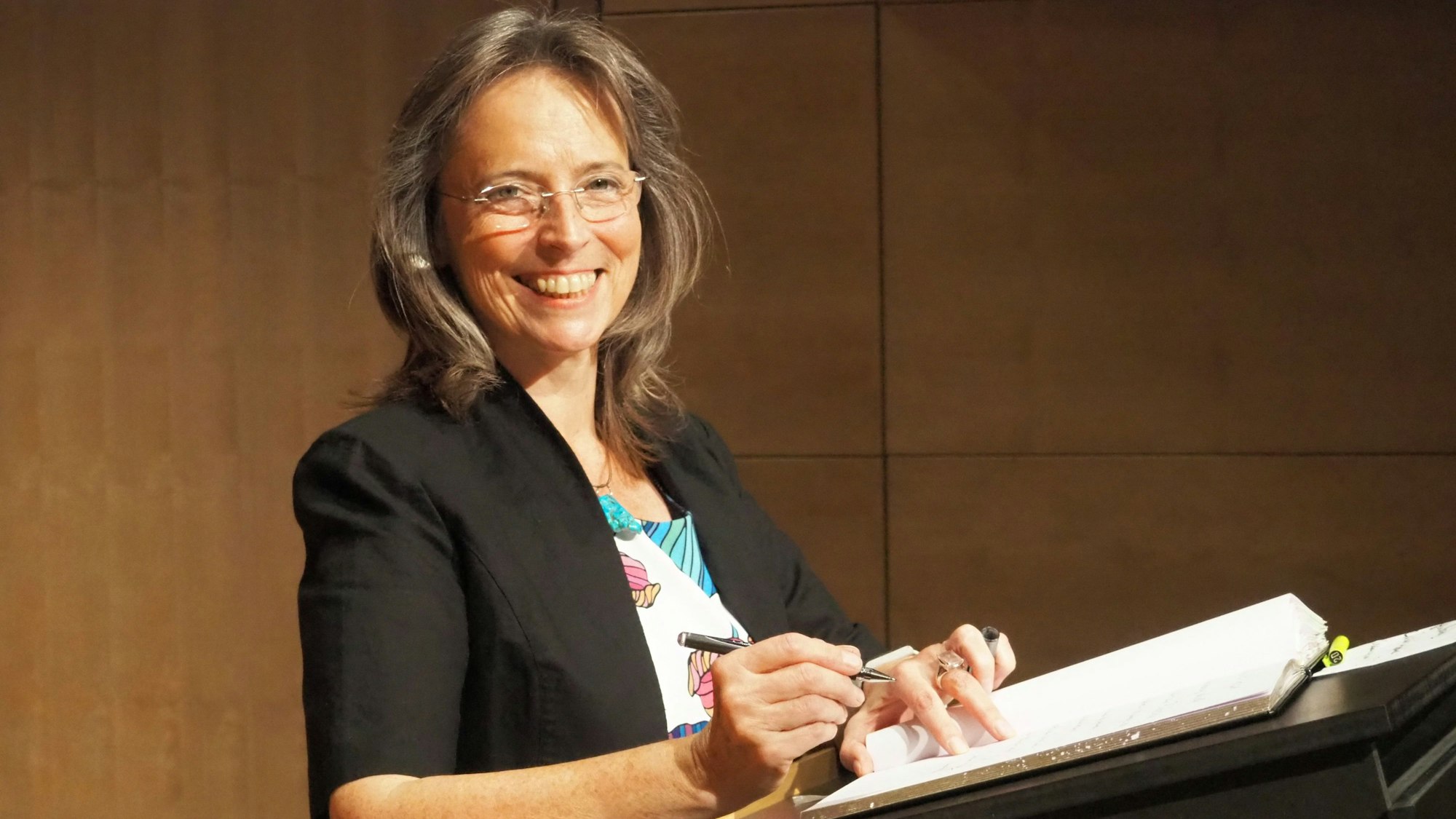Eine Frau steht an einem Rednerpult und unterschreibt auf einem Papier.