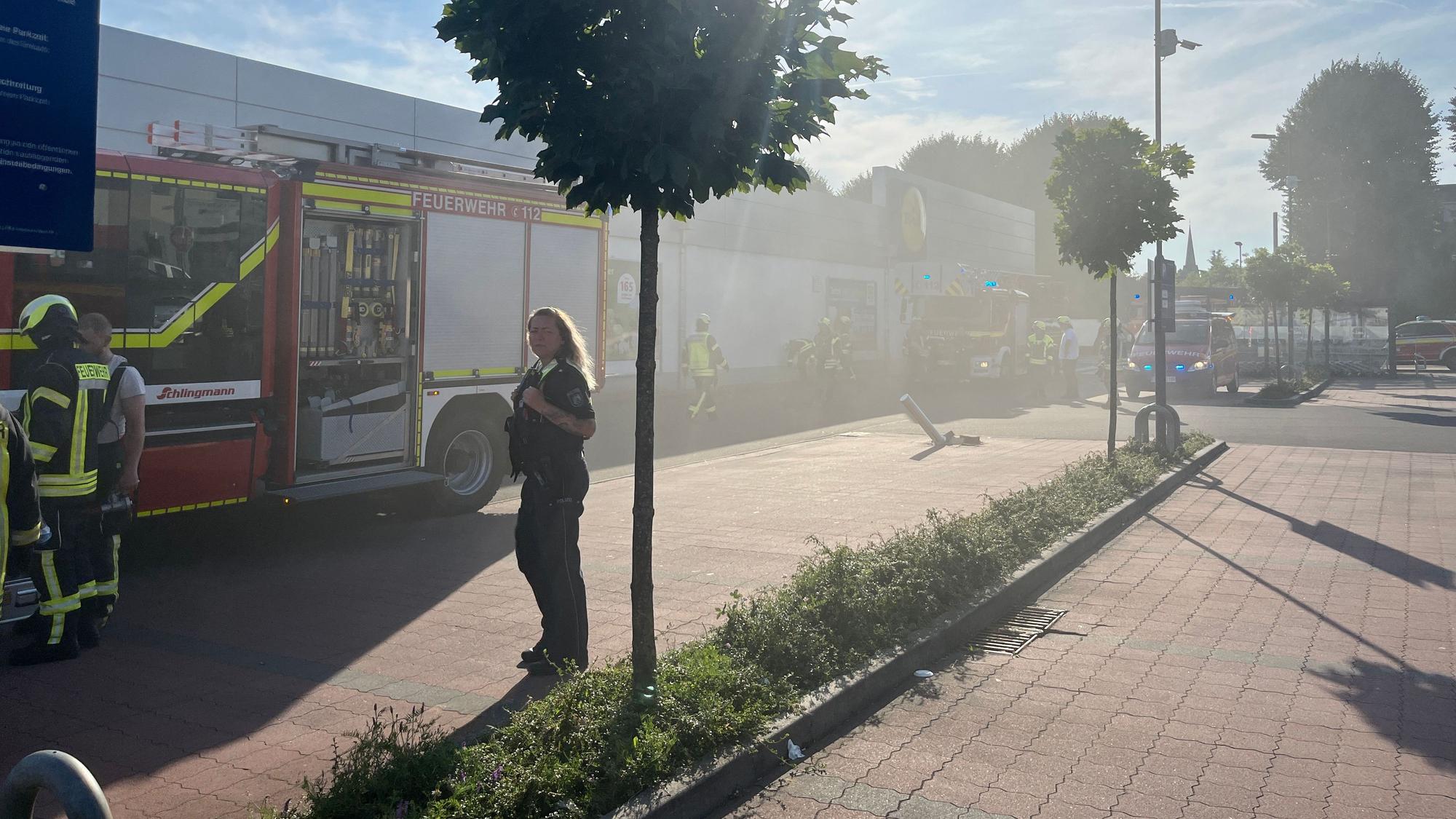 Rauch zieht über einen Parkplatz, auf dem Feuerwehrfahrzeuge stehen.