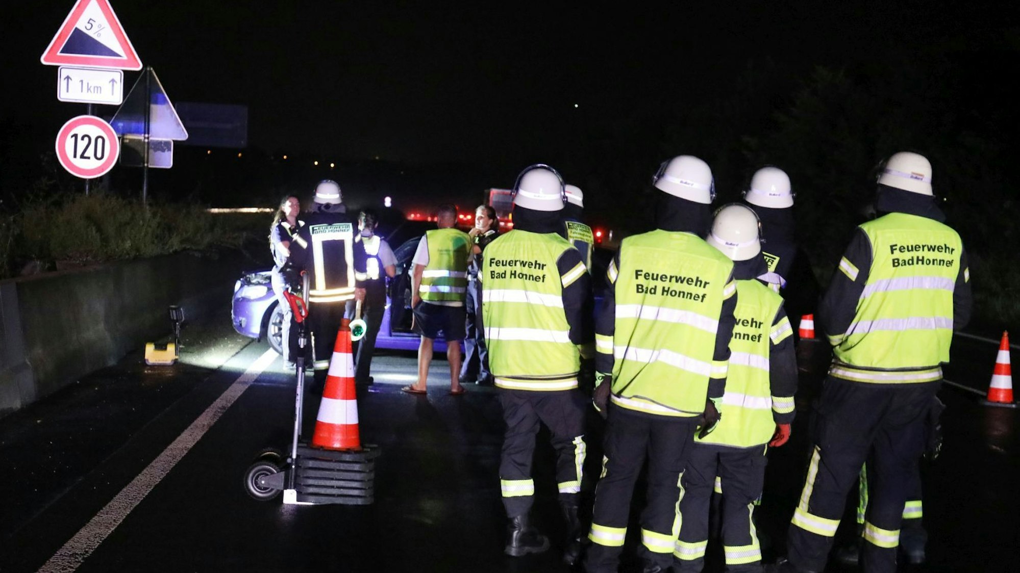 Feuerwehrleute mit Warnwesten stehen auf der Autobahn vor dem Unfallfahrzeug.