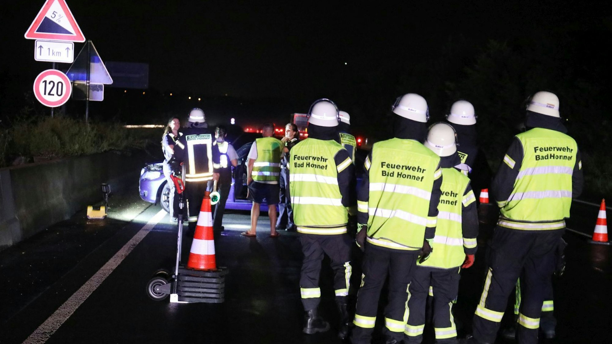 Feuerwehrleute mit Warnwesten stehen auf der Autobahn vor dem Unfallfahrzeug.