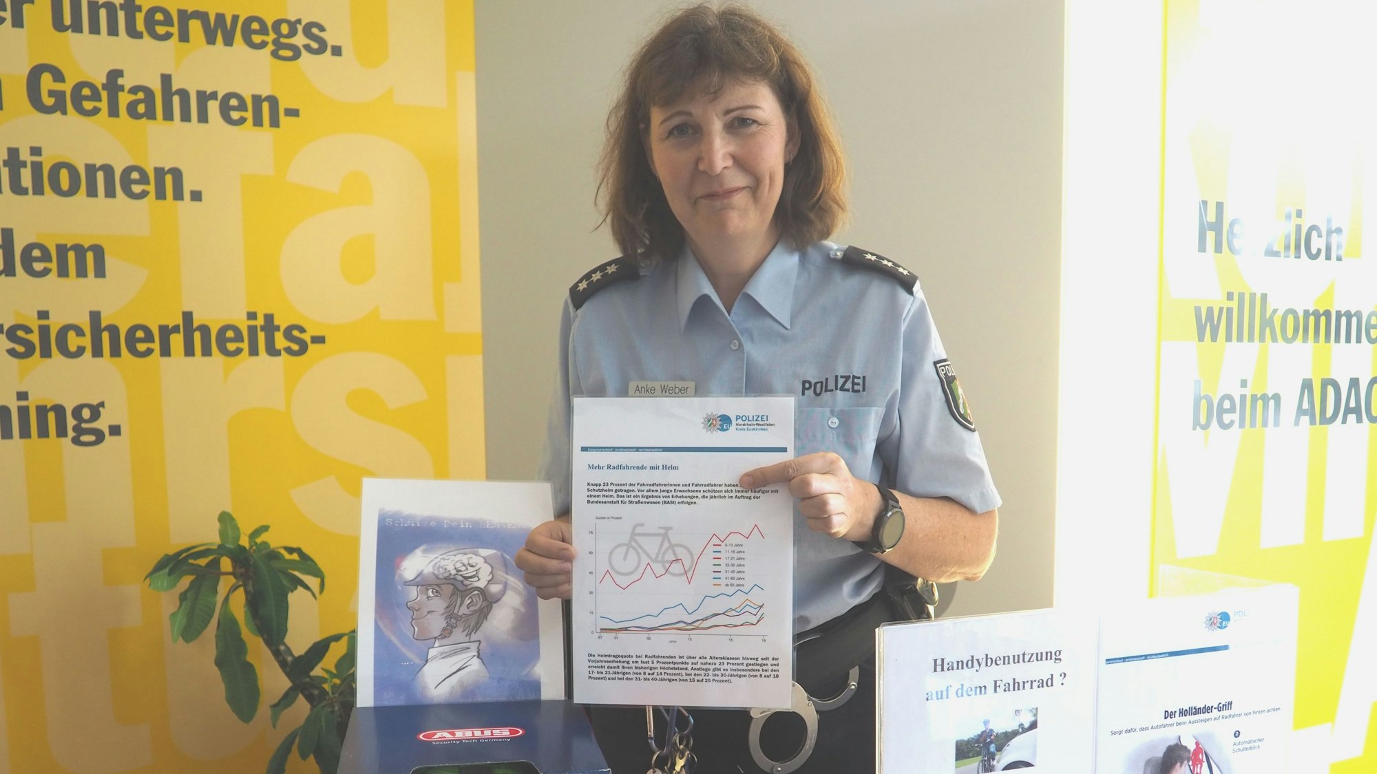 Anke Weber hält eine Grafik in die Kamera, neben ihr sind Informationsbroschüren zu sehen.