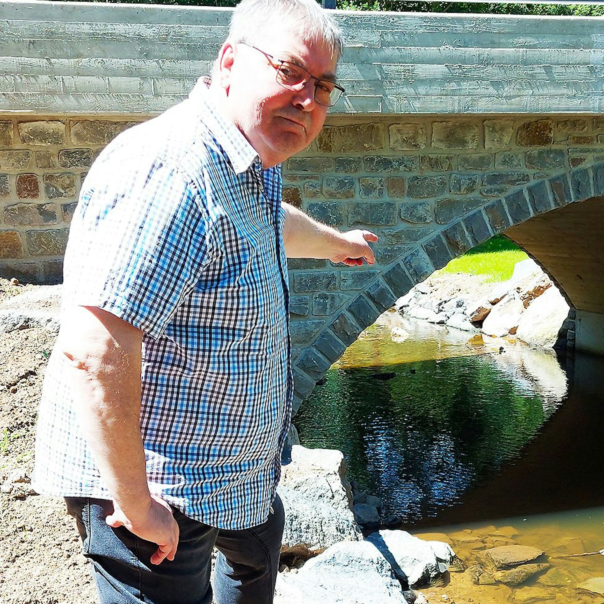 Martin Peetz steht am Rande des Flusses und zeigt auf die Brücke.