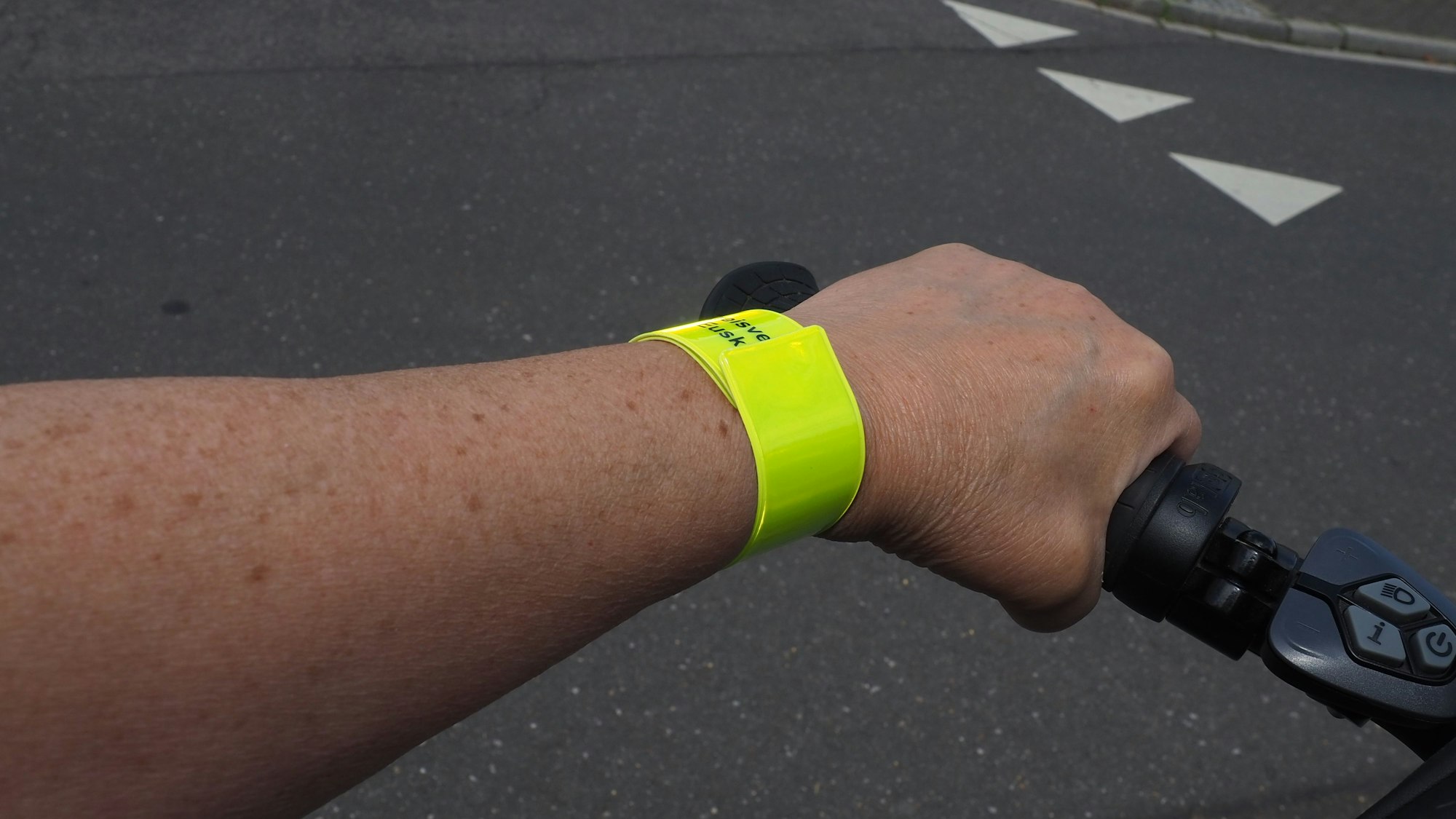 Eine Hand am Fahrradlenker, ums Handgelenk trägt die Frau ein neonfarbenes,. reflektierendes Band.