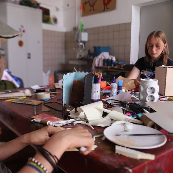 Eine Jugendliche schneidet mit einem Cuttermesser aus Kunststoffplatten einzelne Scheiben, die zu einem Berg zusammengefügt werden.