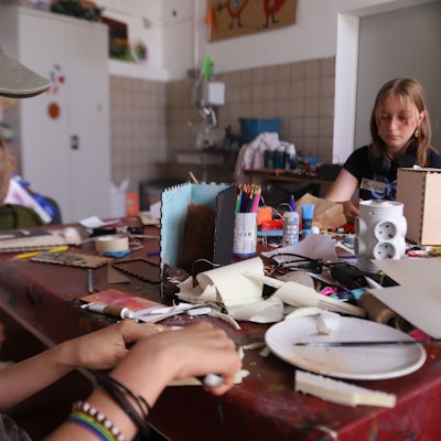 Eine Jugendliche schneidet mit einem Cuttermesser aus Kunststoffplatten einzelne Scheiben, die zu einem Berg zusammengefügt werden.