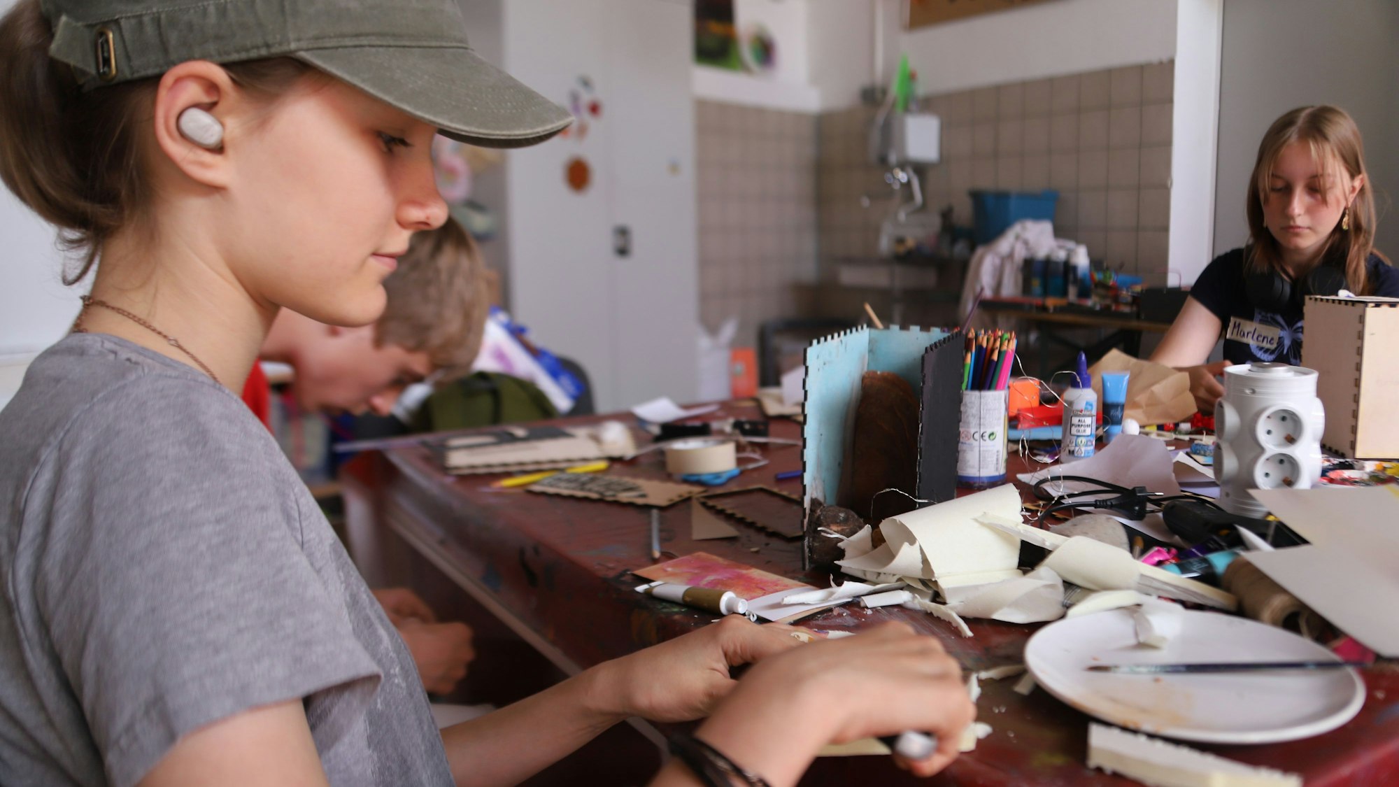 Eine Jugendliche schneidet mit einem Cuttermesser aus Kunststoffplatten einzelne Scheiben, die zu einem Berg zusammengefügt werden.