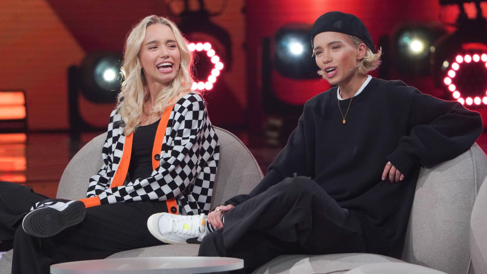 Die Zwillinge Lisa (l.) und Lena sitzen auf einer Couch bei der ARD-Show „Verstehen sie Spaß?“.